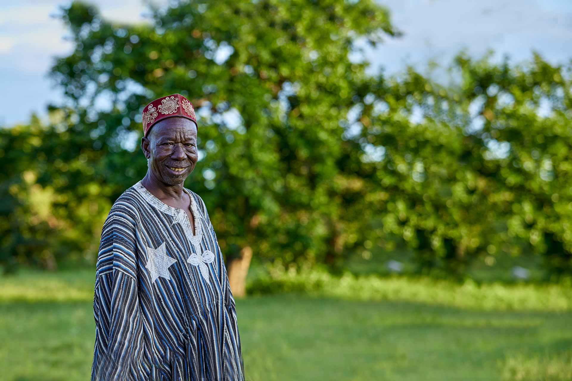 Kazigu, a lead farmer on a Tree Aid project and chief of the village, smiling in front of trees.