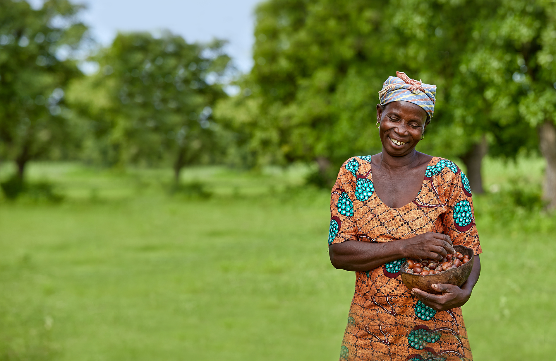 Kubaje, a women that Tree Aid is working with in Ghana, smiling and holding a bowl of shea nuts that she collected.