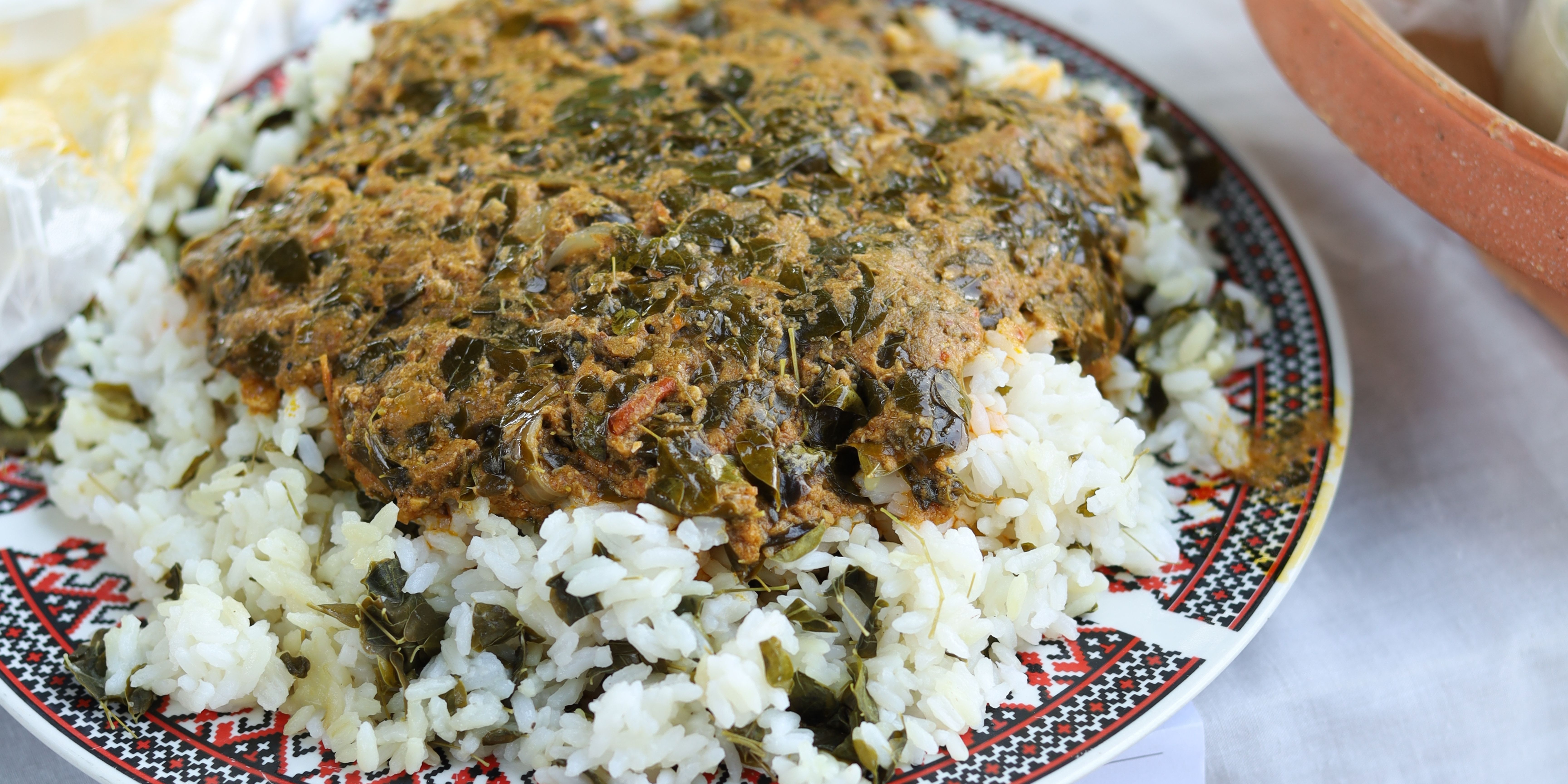 Close up showing a plate of green moringa stew sitting on top of white rice. 