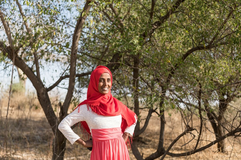 Woman standing in front of tree, smiling and with hands on hips