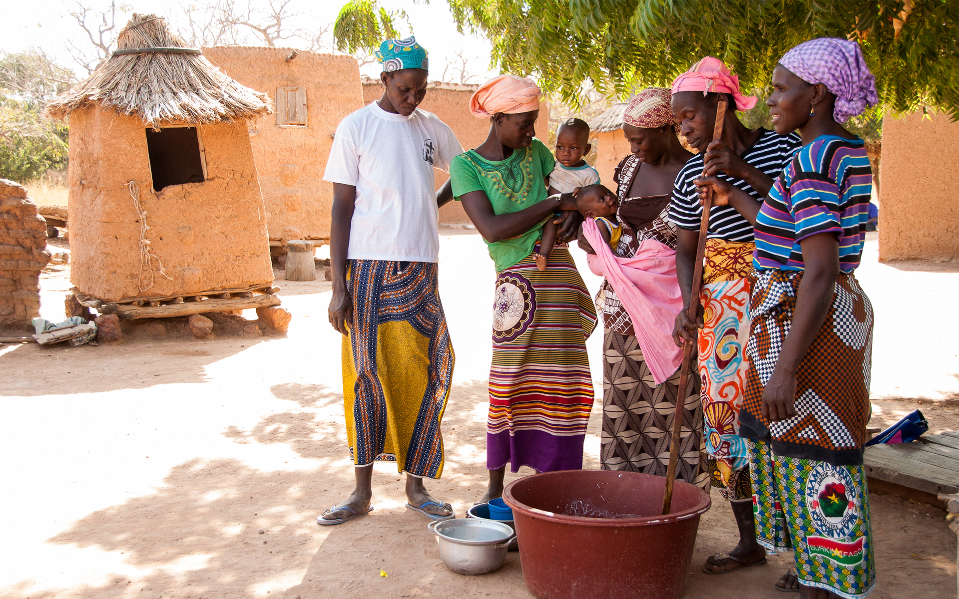 Women from a shea enterprise group in Mali standing round a bowl of shea butter which is being stirred.