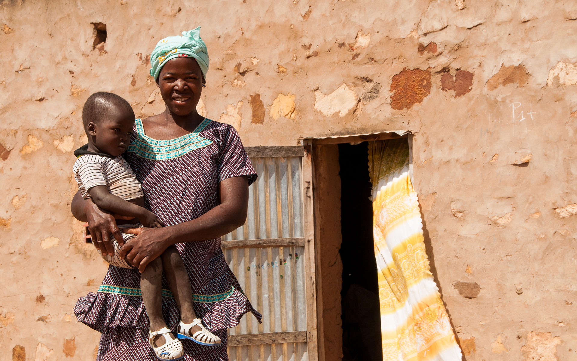 Anè, a women taking part in a Tree Aid enterprise project in Mali, holding her daughter in front of her home.