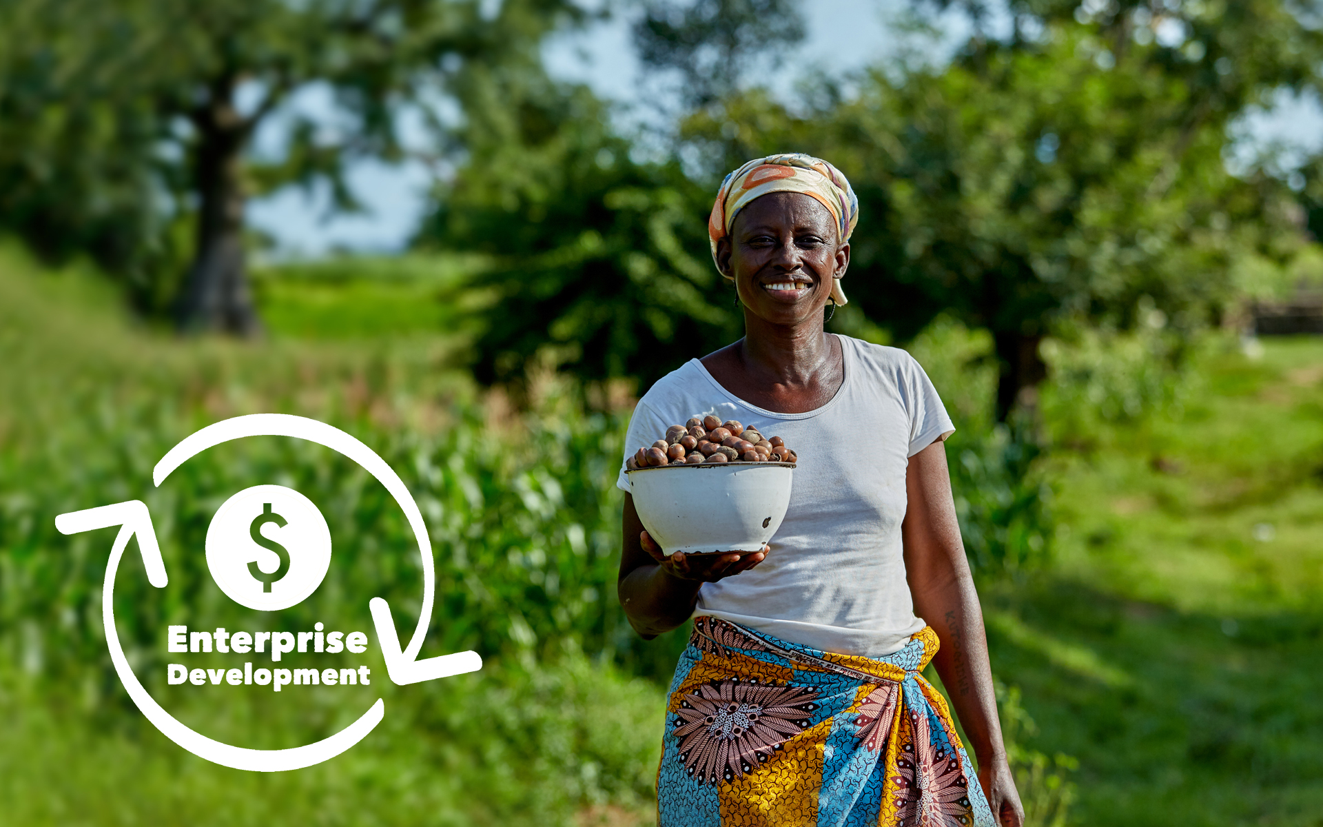 A woman smiling and holding a bowl of shea nuts she has collected.