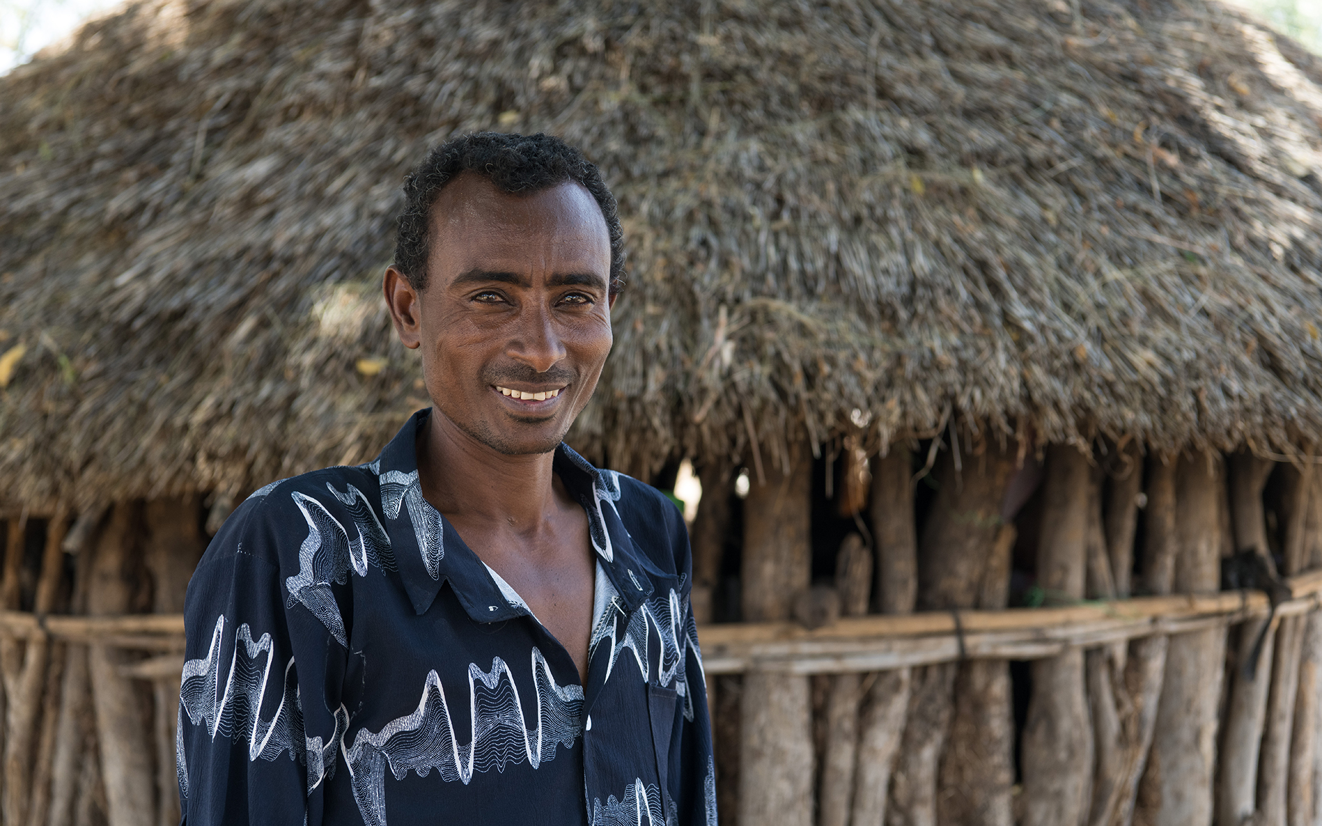 Derese standing and smiling in front of his home in Ethiopia