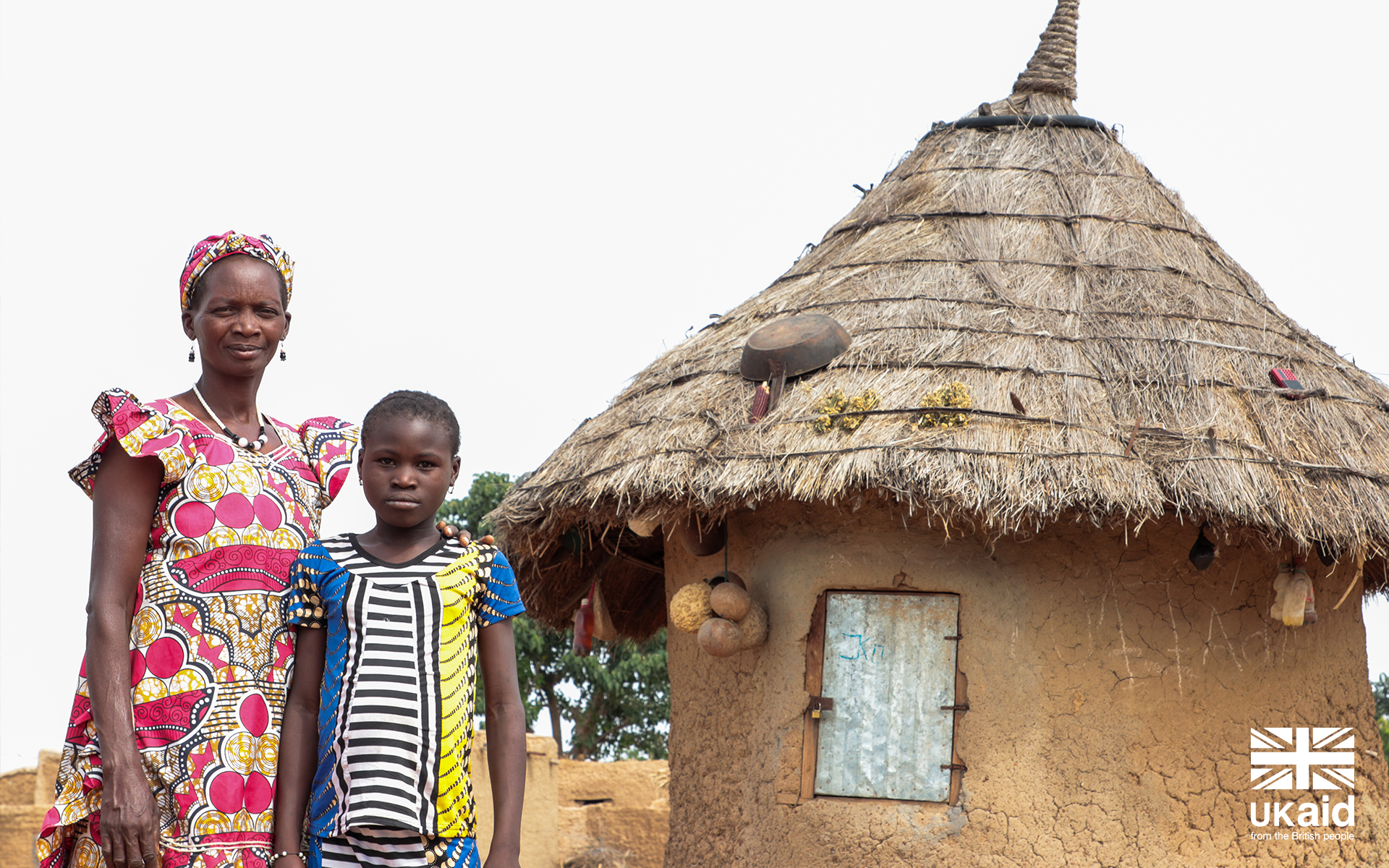 A women in Mali standing in front of her home with her child.