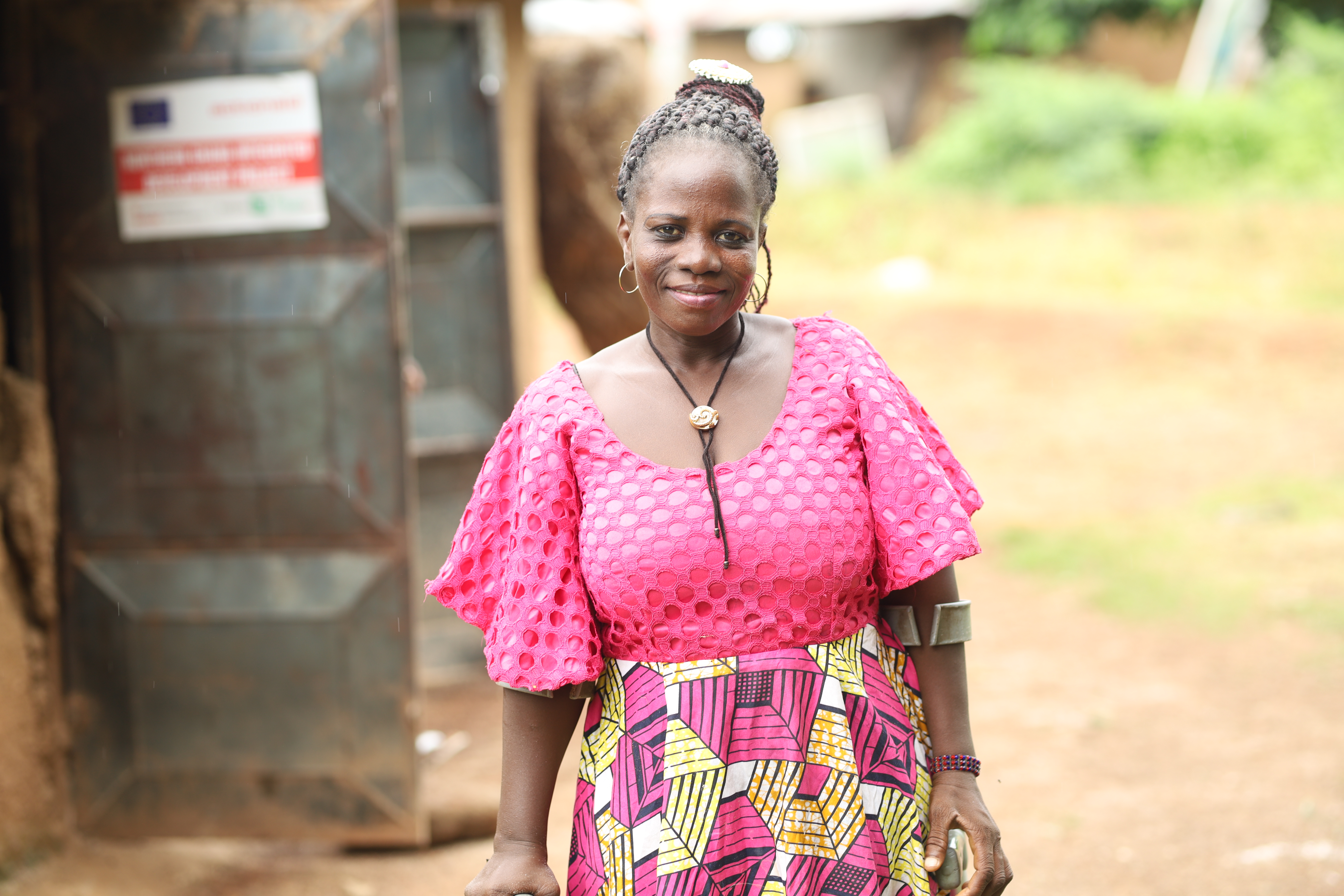 Gifty Amadou, wearing a prink top and a pink and yellow skirt, smiling at the camera and holding a crutch in her left hand