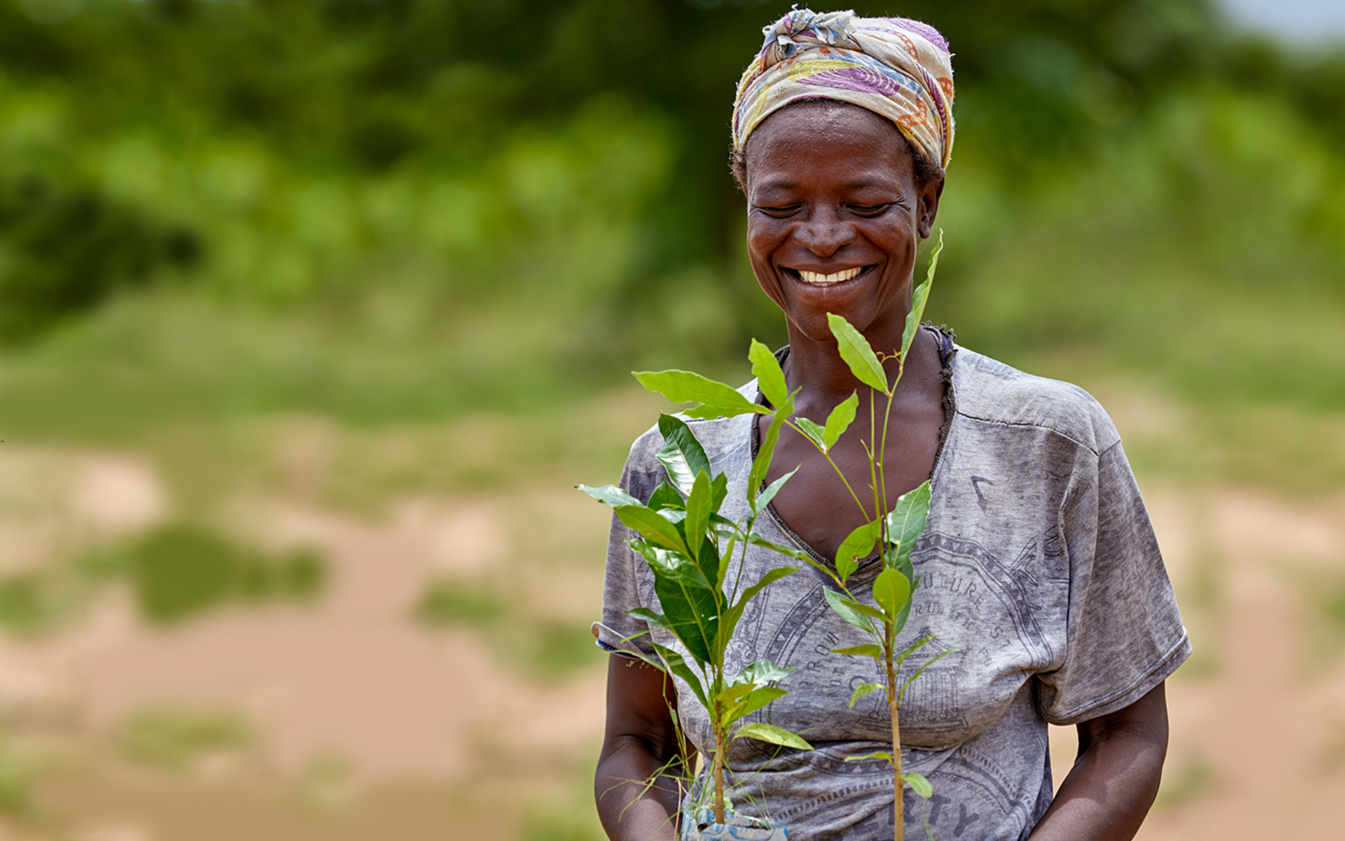 A woman smiling and holding tree saplings which she is about to plant.