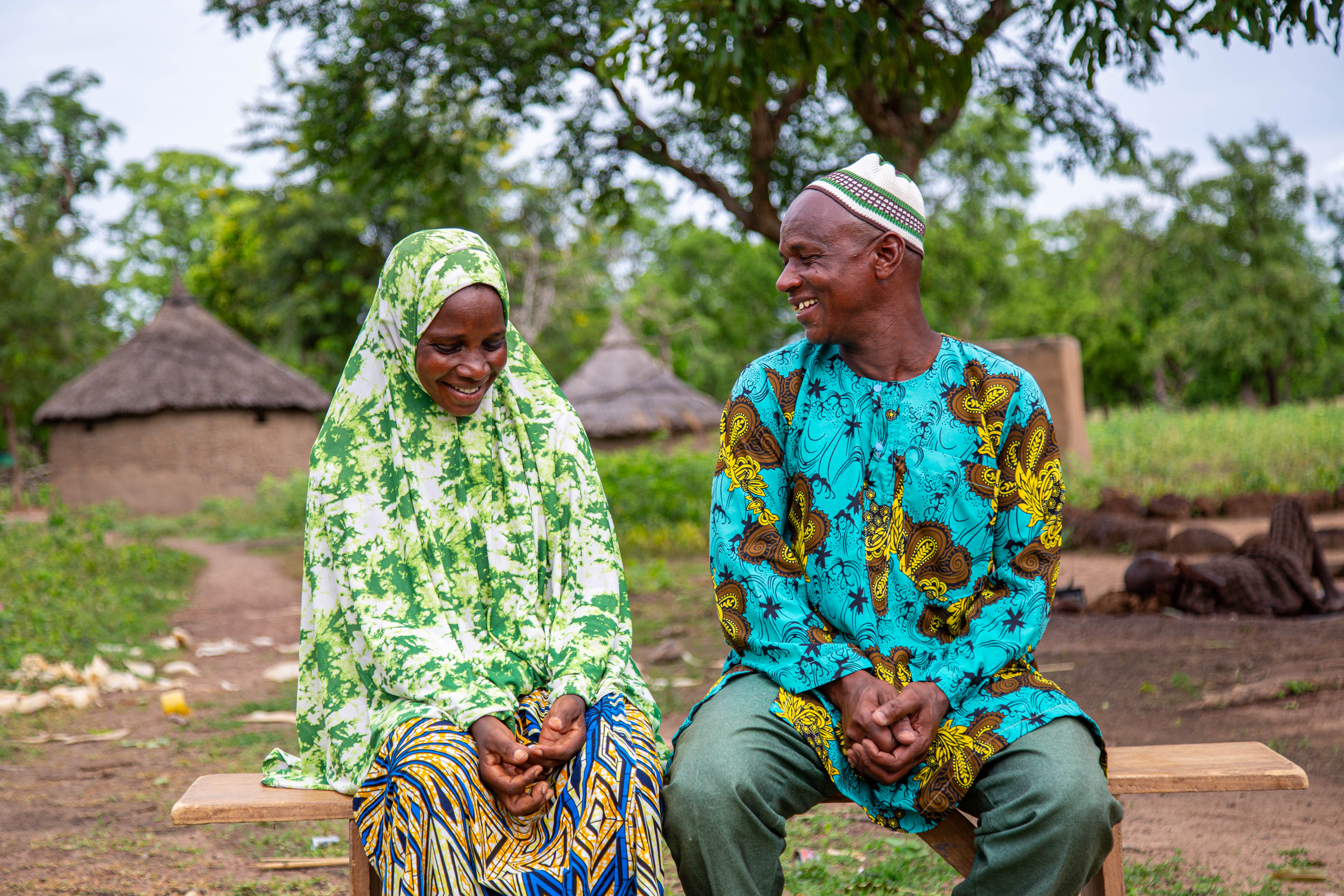 A man and woman sitting on a bench in a forest area, laughing together. 