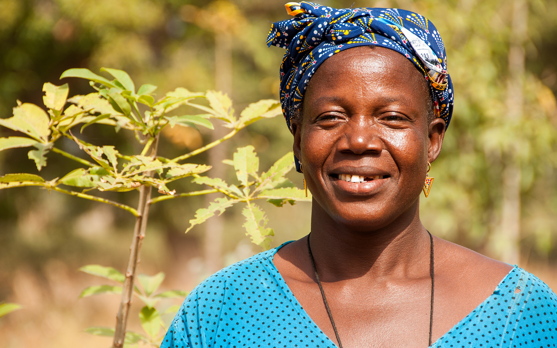 Bernadette, a women in Mali, smiling in front of trees.